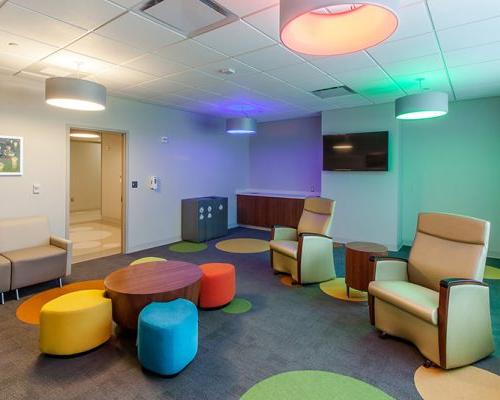 Interior photo of lounge area with colorful lighting, carpeting and seating. Couches line the wall.