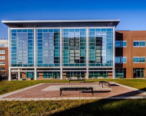 Exterior photo of Maryland Proton Treatment Center during the day. Brick patio with benches are in the middle or a grassy area.